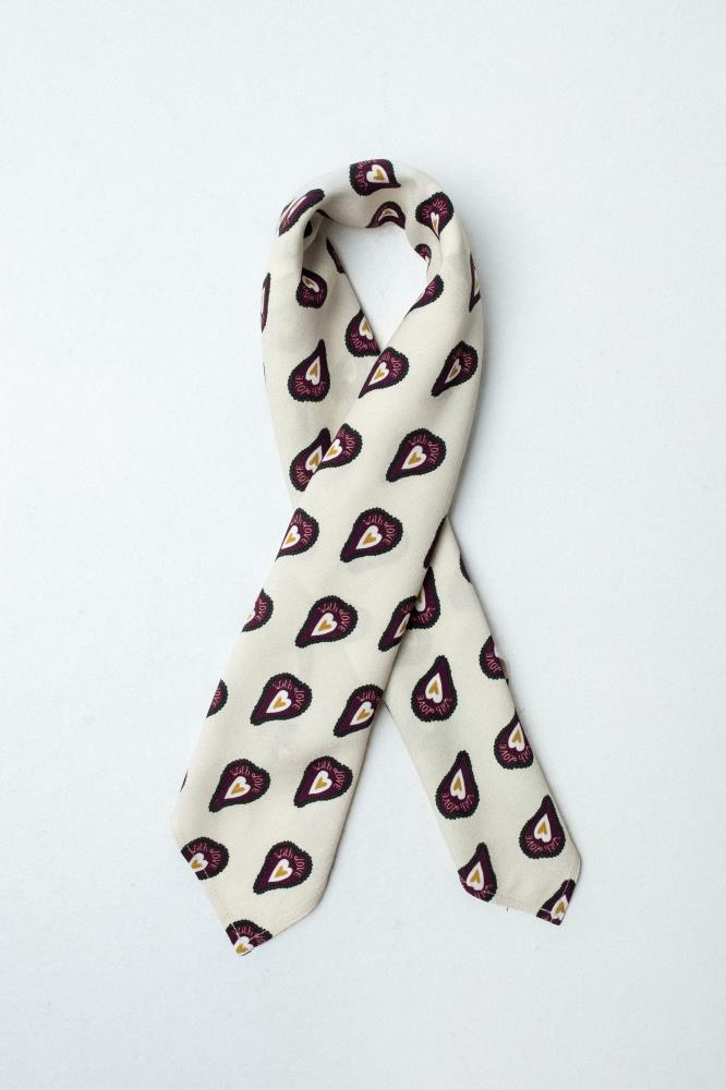 a square, light-colored fabric scarf, artfully folded into a narrow, long strip and looped. It is laid against a clean white background. The accessory features a repeating pattern of dark burgundy shapes, each with a yellow heart and the text "With LOVE" inside.