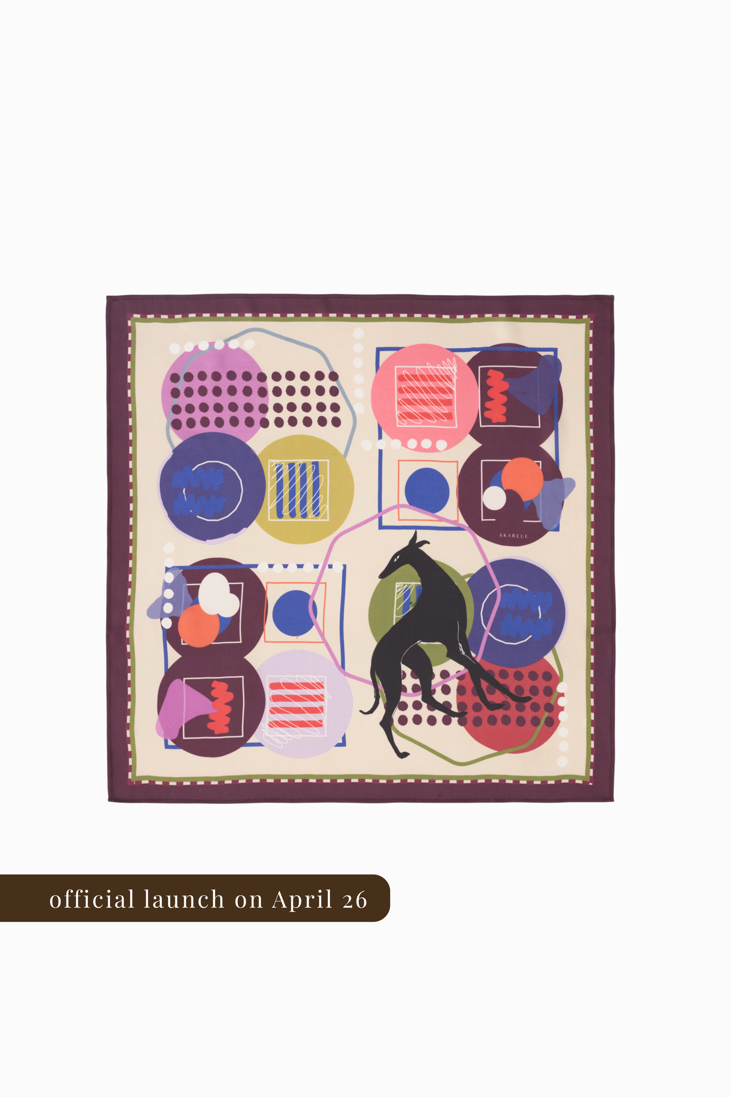 A top-down view of a square silk scarf featuring a full abstract print with a central black greyhound silhouette. The design is composed of four quadrants with various geometric shapes, dots, and lines in pink, purple, and olive green on a cream background. It is framed by a deep plum border. A brown banner at the bottom indicates the official launch on April 26.