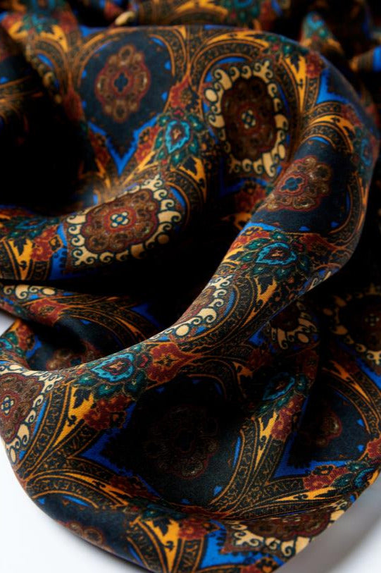 Extreme close-up of a premium silk scarf, showcasing its rich paisley pattern and vibrant blue and gold tones with a soft, lustrous sheen.