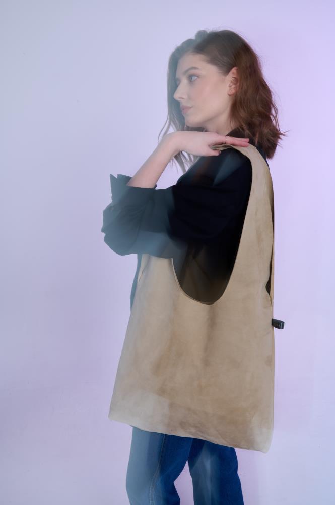 Artistic profile shot with a dreamy, blurred effect of a woman showcasing a large sand-colored suede tote bag for a modern, ethereal fashion aesthetic.