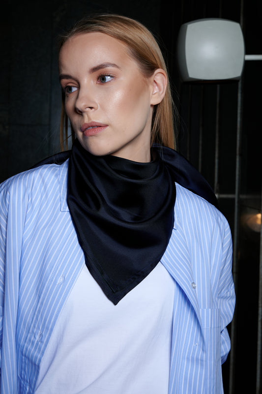 A woman with light hair gazes to the side, wearing a blue striped shirt and a midnight blue silk bandana style. The dimly lit background adds a contemplative mood.