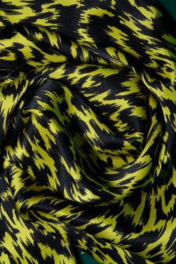 Texture of a yellow and black abstract patterned silk scarf. The photograph focuses on the soft drapes and satin finish of the luxurious material.
