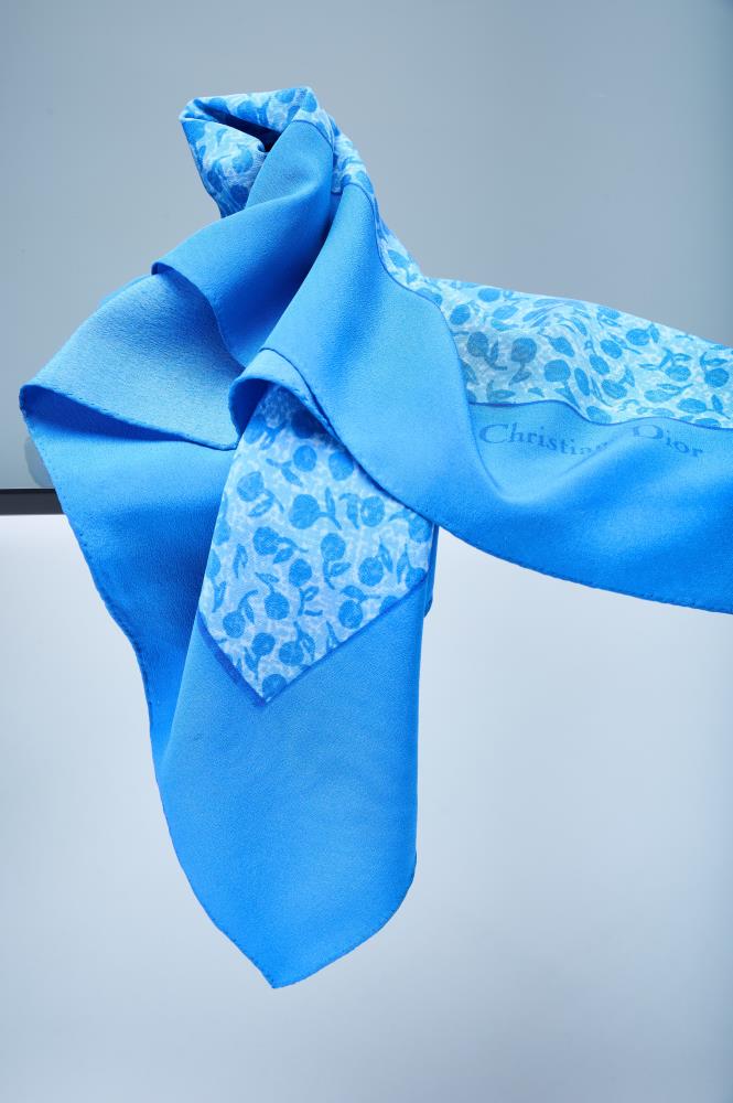 Close-up of a premium blue silk scarf, showcasing the iconic logo, delicate floral print, and the soft, elegant drape of the high-quality fabric.
