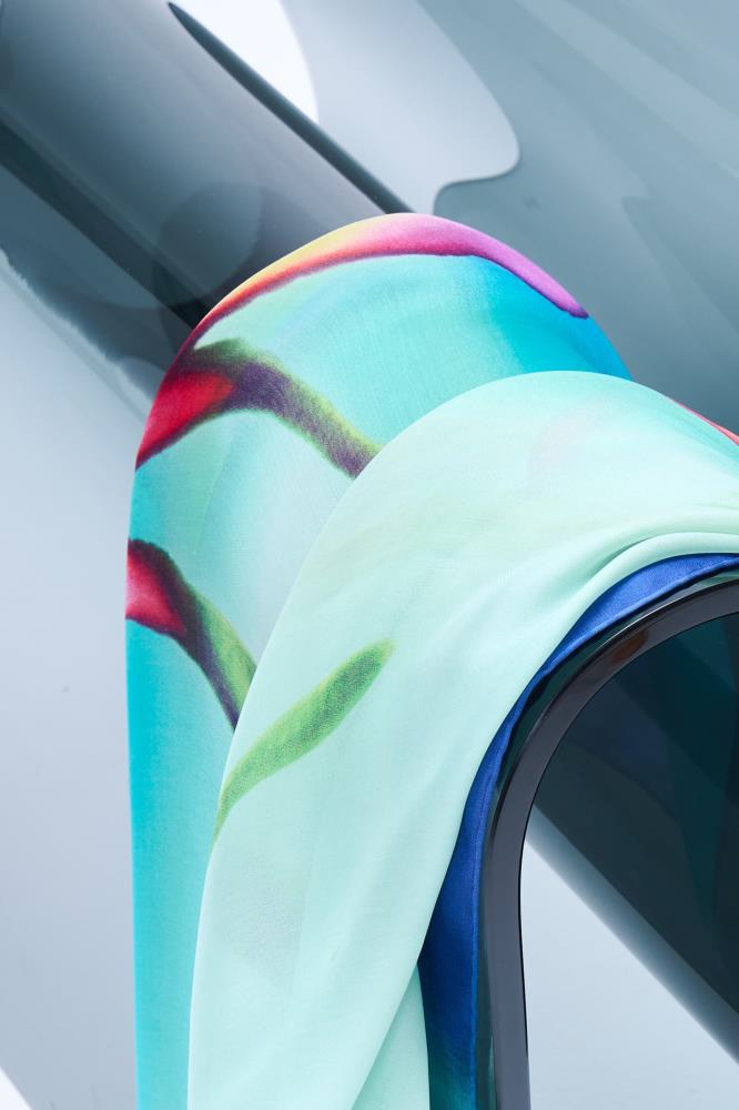 close-up of a Christian Lacroix silk scarf with a vibrant floral print in turquoise, mint green, and magenta, draped over a modern glass surface.
