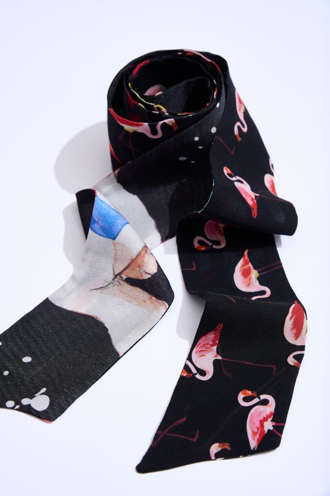 A coiled black "Twilly" silk scarf with a double-sided design on a white background. The photo clearly shows the pink flamingo pattern on one side and colorful space motif details on the other. The soft sheen of the fabric and the unique print highlight the quality and style of this modern accessory.