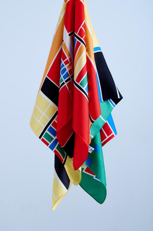 Detailed view of a draped luxury scarf showcasing an abstract graphic pattern in striking primary colors, highlighting the high-quality silk fabric texture and smooth satin sheen.