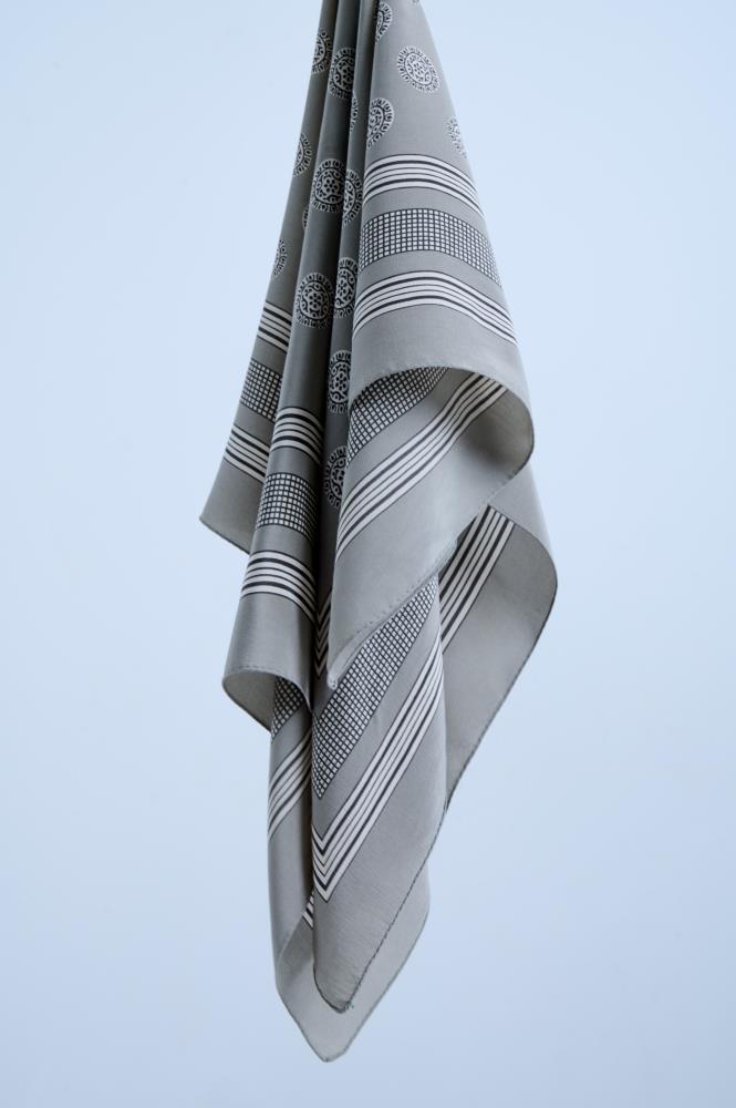 A high-quality grey silk scarf with a classic pattern featuring black and white stripes, circular medallions, and a fine grid motif, artfully draped to showcase the fluid fabric and sophisticated design.