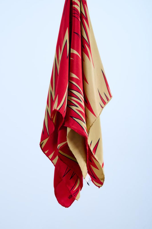 A vintage silk scarf in red and caramel colors with rolled and tucked edges, hanging against a white background.