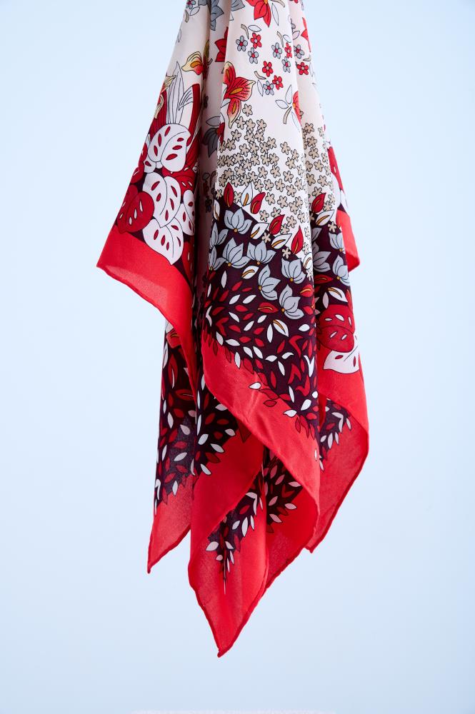 Close-up of a draped silk scarf with a vibrant red and white botanical print, featuring monstera leaves and delicate floral patterns with a bold red border, shot in a professional studio.