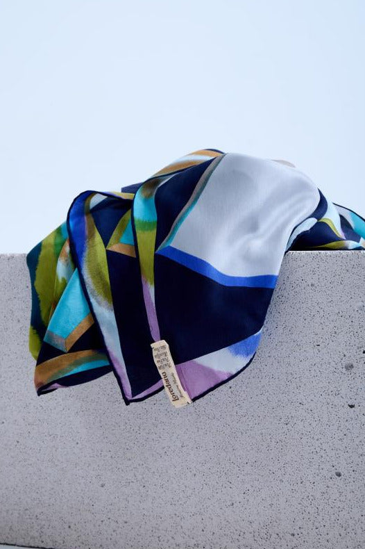 Close-up of silk scarf, highlighting the high-quality fabric sheen, intricate colorful geometric print, and authentic brand label in a studio setting.