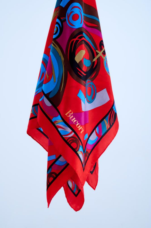 Close-up of a high-quality red silk scarf with a modern abstract geometric print in blue, teal, brown, and magenta