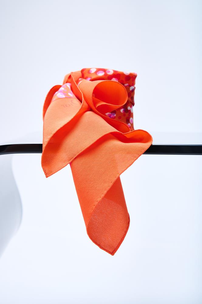 Artistic display of a premium orange designer scarf, showcasing the fluid drape and soft texture of the silk fabric alongside an intricate multicolored confetti pattern