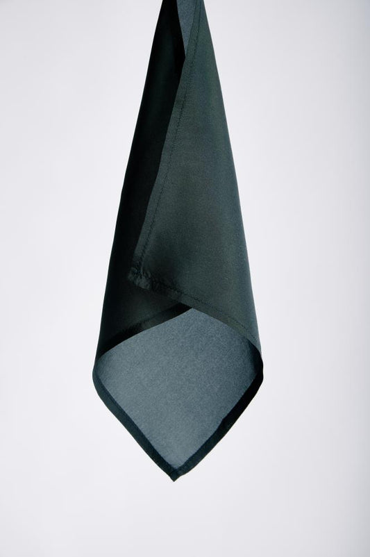 A dark green, pocket square/ handkerchief with a smooth texture hangs elegantly against a plain gray background, conveying simplicity and sophistication.