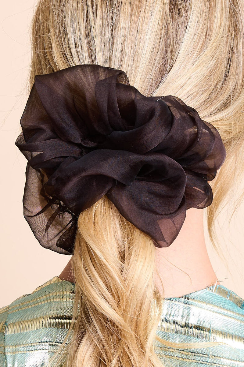 A woman from behind with her blonde hair tied in a ponytail. The hair is secured with a large burgundy silk scrunchie featuring a darker pattern. She is wearing a shimmering blue and gold striped top