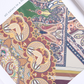 A fragment of a silk scarf featuring a highly detailed and colorful bohemian pattern. The design intertwines oriental paisley motifs, stylized flowers, and ornaments, harmoniously combining rich green, burgundy, mustard, and cream tones. The text "all colors in a fine pattern" in the photo highlights the intricacy of the print and the elegance and high quality of the accessory.