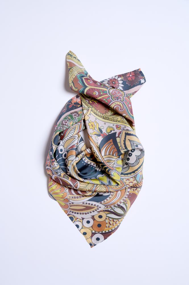 A colorful silk scarf artistically draped and knotted on a clean white background. The fabric features an intricate paisley and floral pattern with a vibrant palette of ochre, teal, burgundy, and cream. The elegant folds and soft sheen of the material highlight the luxurious silk texture, creating a dynamic and sophisticated composition.