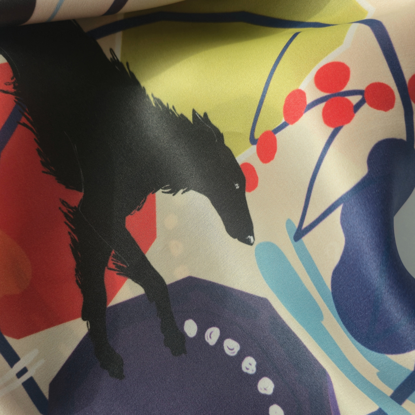 A close-up of a printed silk scarf pattern featuring borzoi dog silhouette over abstract shapes in red, blue, yellow, and cream.