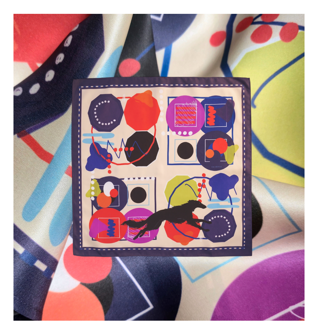 A square graphic featuring the Skarele Borzoi Edition silk scarf centered over a blurred macro background of its own draped, colorful satin fabric pattern with vibrant geometric shapes.