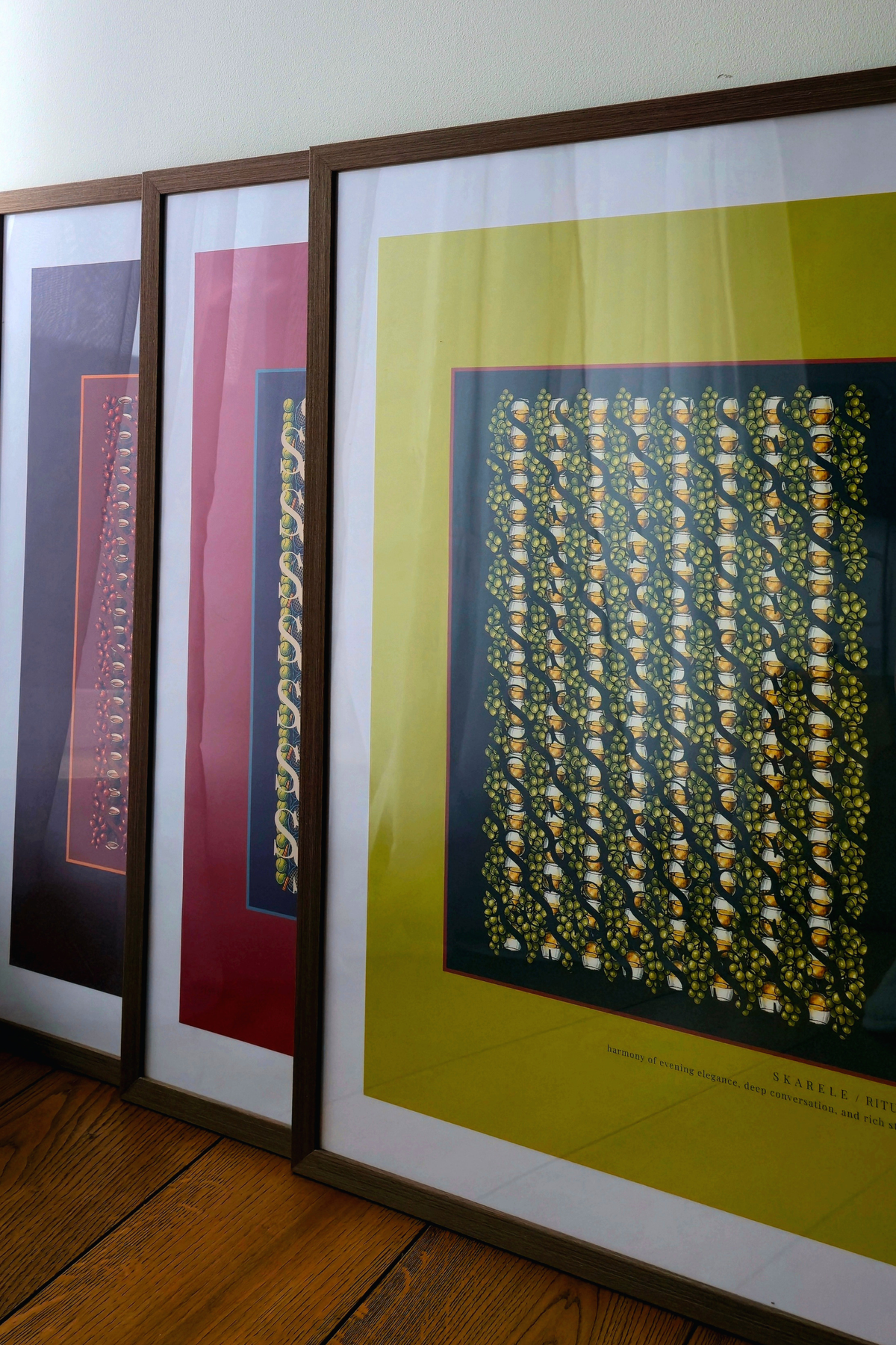 Trio of framed "Skarele / Rituals" digital art prints in matching dark wooden frames, showing colorful poster designs in pistachio green, deep red, and dark purple arranged together in an interior setting