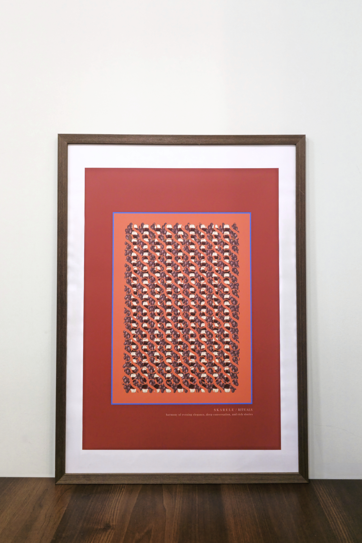 Interior mockup of the "Evening deep red" digital poster framed in a thin dark wooden frame with a white passe-partout mat, resting on a wooden table against a clean white wall.