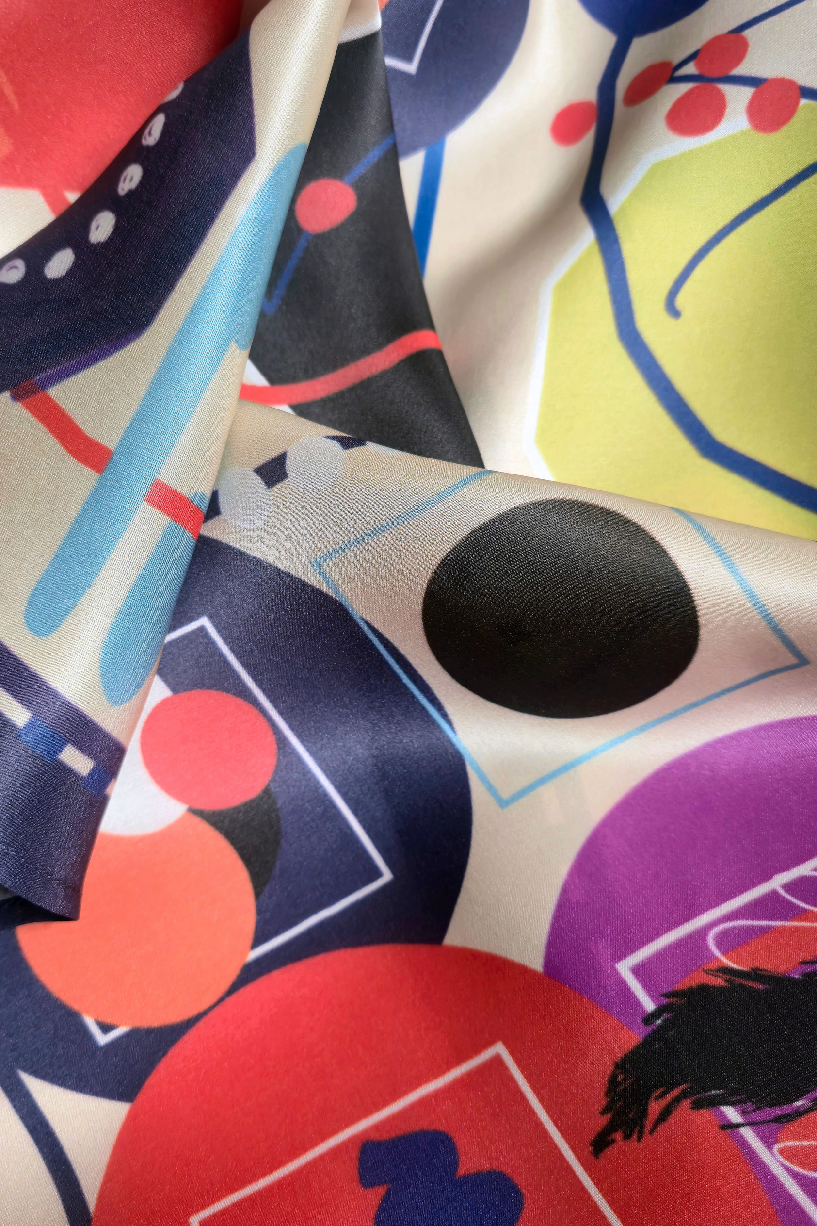 Detailed macro view of premium silk scarf fabric texture. Abstract modern graphic design with vibrant red, purple, and green circles from the Skarele luxury accessory collection.
