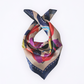 Elegant draped Borzoi Edition silk scarf tied in a loop. Features a cream base with vibrant abstract geometric prints and a dark blue purple dashed border on a clean white background.