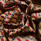 A close-up of crumpled silk fabric with a bold geometric pattern. The fabric intertwines rich red, gold, and black colors, forming sequences of diamonds and stylized ornaments. The glossy silk surface and deep folds create a sense of luxury and dynamism, highlighting a classic design with a touch of oriental motifs.