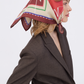 Side profile of a woman wearing the MUSE Chestnut Brown Silk Scarf tied elegantly over her head. The scarf features a sophisticated geometric pattern with chestnut brown, cream, and bold red accents. She is styled in a textured chocolate brown blazer against a clean white background.