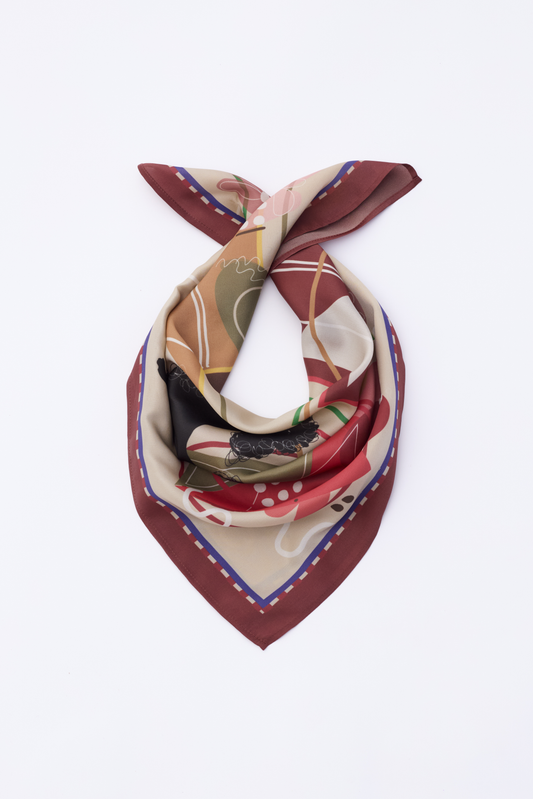 A flat lay view of the MUSE Chestnut Brown Silk Scarf, elegantly twisted to highlight its intricate abstract pattern. The design includes artistic sketches of figures and geometric shapes in earthy tones. The chestnut brown edges frame the multi-colored center, emphasizing the luxurious quality and modern artistic aesthetic of the silk accessory.