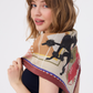 Detail of the MUSE Silk Scarf in Chestnut Brown, showcasing a whimsical black poodle silhouette as part of its modern abstract print. The scarf's creamy base is decorated with geometric lines and earthy tones, styled as a chic shoulder wrap. The image highlights the artistic storytelling and playful design of the accessory.