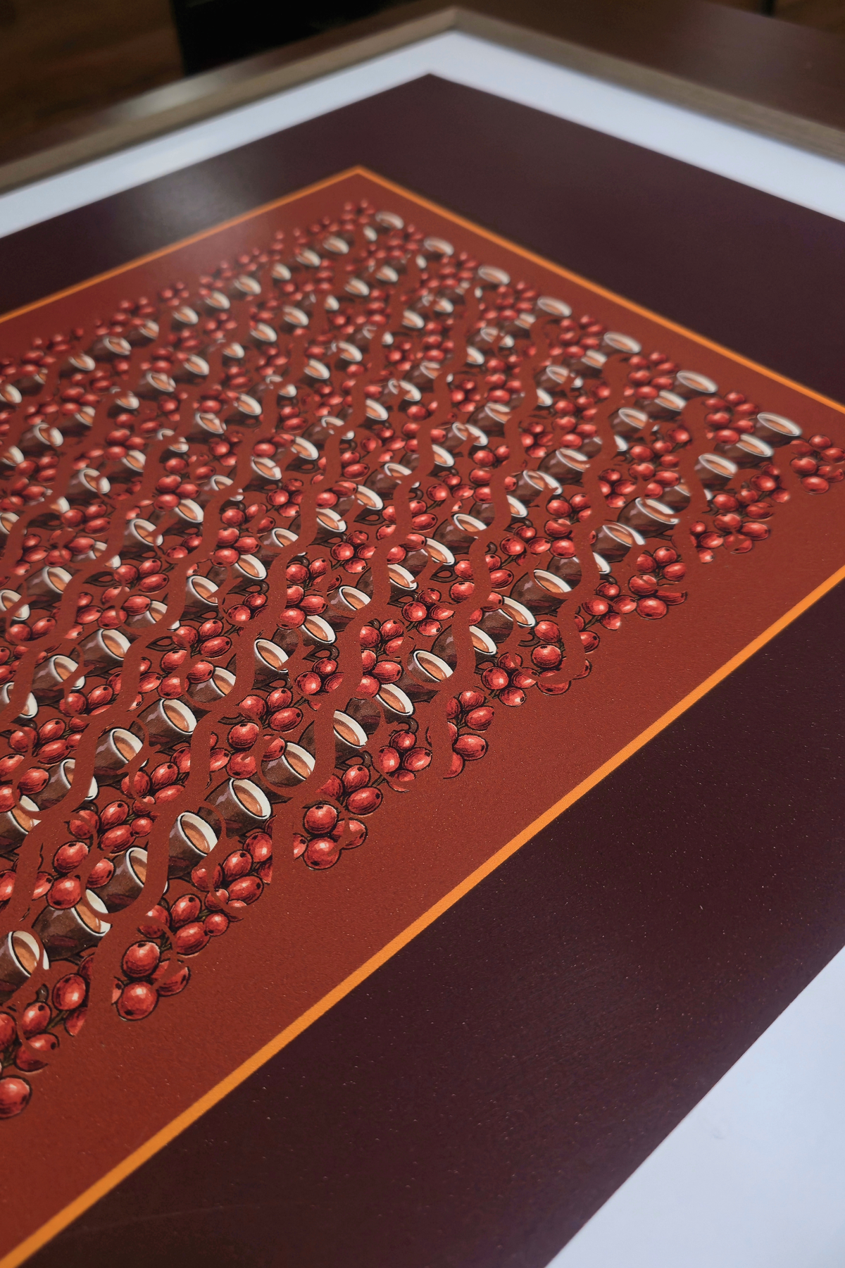 Perspective view close-up of the "Morning bordeux" art print, highlighting the print finish, amber inner frame, coffee cups, and red berry clusters set within a wooden frame
