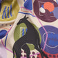 Macro shot of the NOMAD Silk Scarf in Velvet Plum, highlighting the rich colors and playful abstract pattern. The image showcases the sleek black sighthound silhouette surrounded by mid-century modern geometric elements in magenta, coral, and deep purple. The soft drapes of the luxury silk fabric emphasize its high-quality feel and fluid movement, making it a standout fashion accessory.