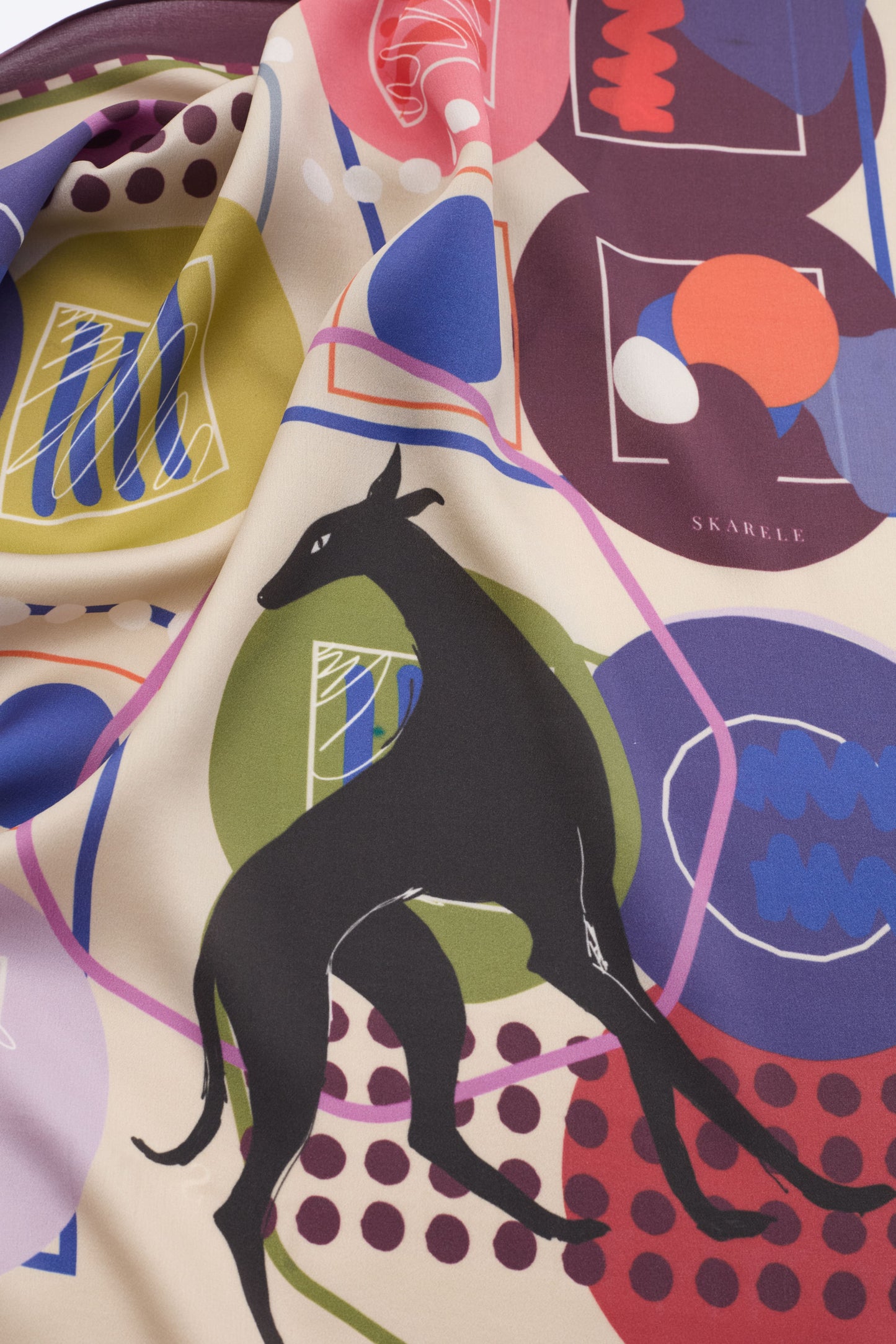 Macro shot of the NOMAD Silk Scarf in Velvet Plum, highlighting the rich colors and playful abstract pattern. The image showcases the sleek black sighthound silhouette surrounded by mid-century modern geometric elements in magenta, coral, and deep purple. The soft drapes of the luxury silk fabric emphasize its high-quality feel and fluid movement, making it a standout fashion accessory.
