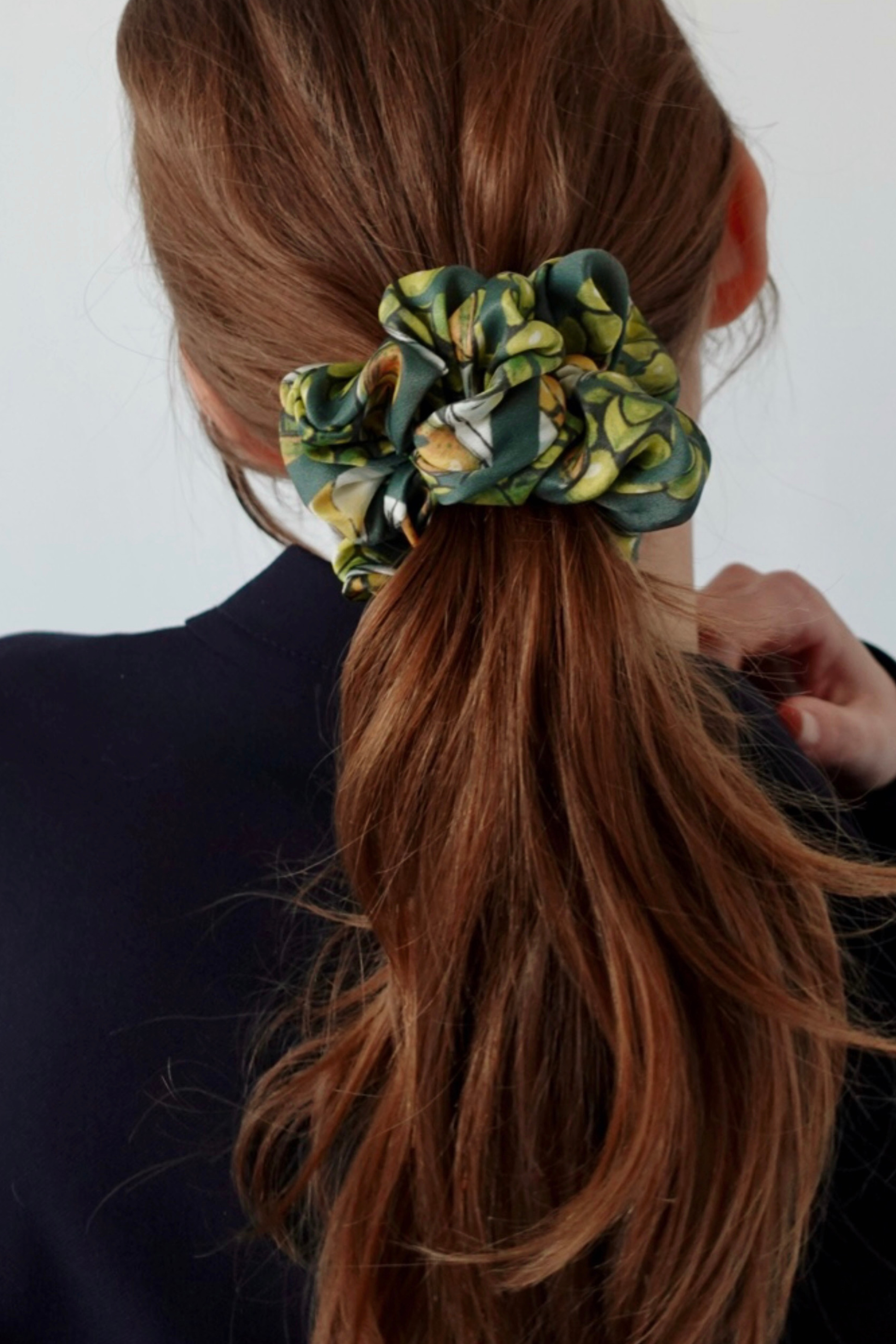 Person with a ponytail held by a pistachio green scrunchie against a white background