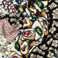 A close-up of crumpled fabric with a vibrant, mosaic-like pattern. The design features various geometric shapes, floral motifs, and ornaments in a palette of white, black, yellow, green, and burgundy. The folds create a dynamic play of shadows and highlight the intricate details of the pattern.