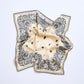 A beige and black bandana-style viscose scarf laid out flat with paisley patterns.