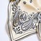 A close-up image of a viscose scarf with a floral and paisley pattern in black and beige colors.
