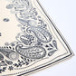 A close-up of the corner of a light cream-colored scarf laid against a white background. The photo highlights the detailed black paisley pattern, consisting of elegant lines, dots, and botanical motifs