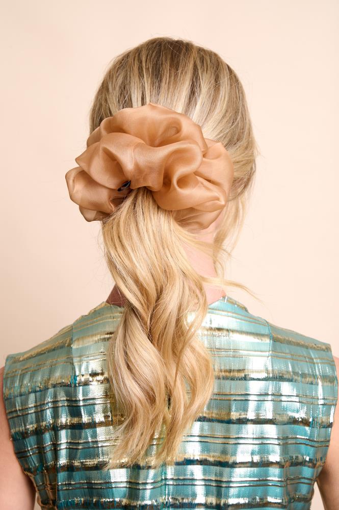 A woman with a peach-colored silk scrunchie in her hair, wearing a turquoise and silver patterned dress.