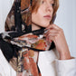 Woman in a white blazer gazes upward, wearing a patterned scarf with earthy tones. The image conveys elegance and introspection.