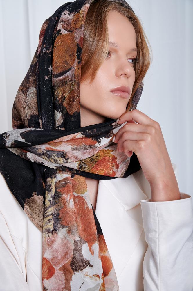 Woman in a white blazer gazes upward, wearing a patterned scarf with earthy tones. The image conveys elegance and introspection.