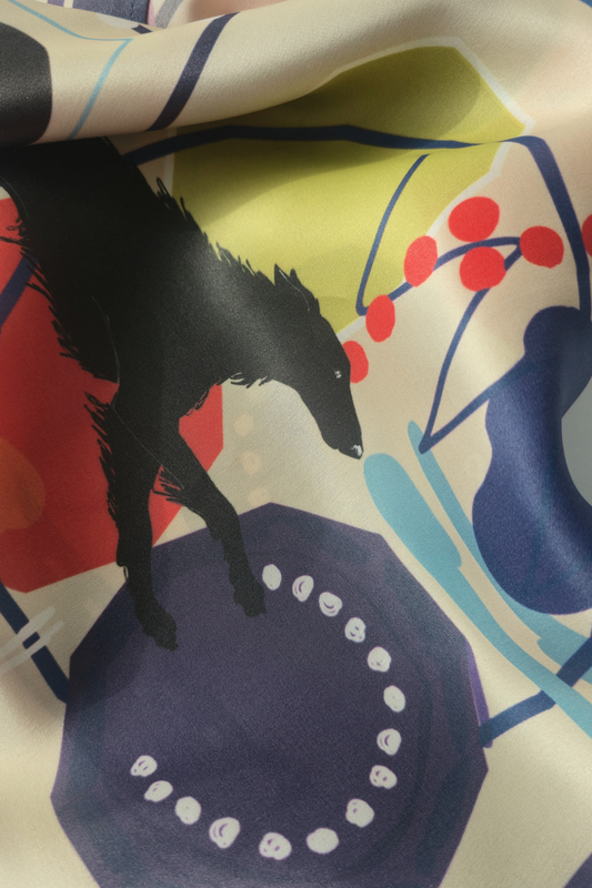 A close-up of a printed silk scartf with an abstract multicolor design featuring a black borzoi silhouette, red dots, blue and yellow shapes, and a cream base.
