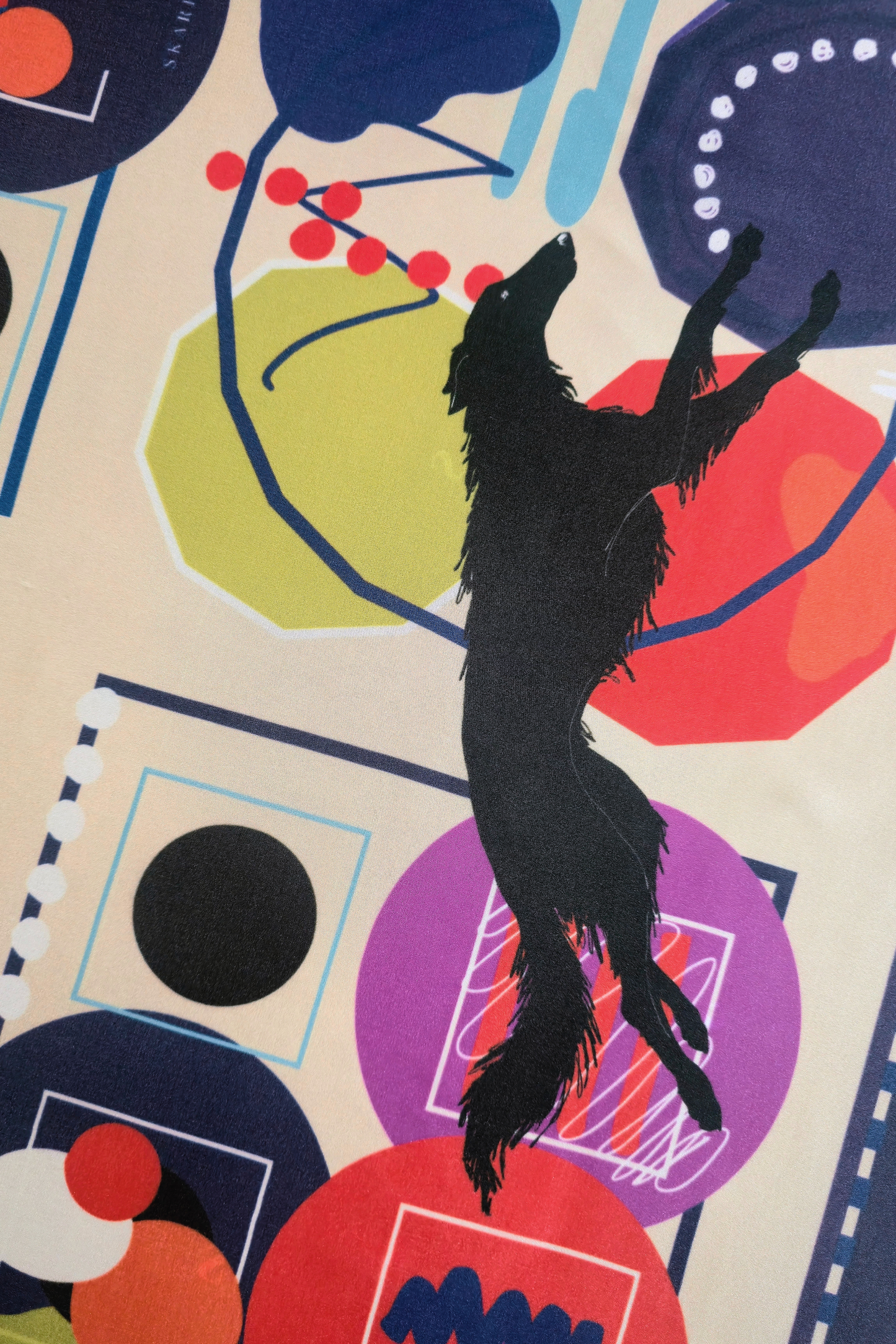 Macro view of a luxury silk scarf print. Illustrates a playful black Borzoi dog silhouette surrounded by modern abstract art shapes, red dots, and colorful circles on a cream background.