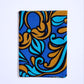 A rectangular folded piece of fabric placed vertically against a clean white background. The material features a large, decorative pattern with royal blue, cyan, and bronze motifs, outlined in bold black contours.