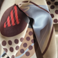 A close-up of a silk scarf with a modern abstract print featuring brown polka dots, a red striped motif, and a light blue wave on a beige background.