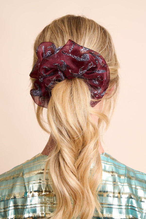 Person with a braided hairstyle wearing a large silk organza hair scrunchie in burgundy with small cheetah details