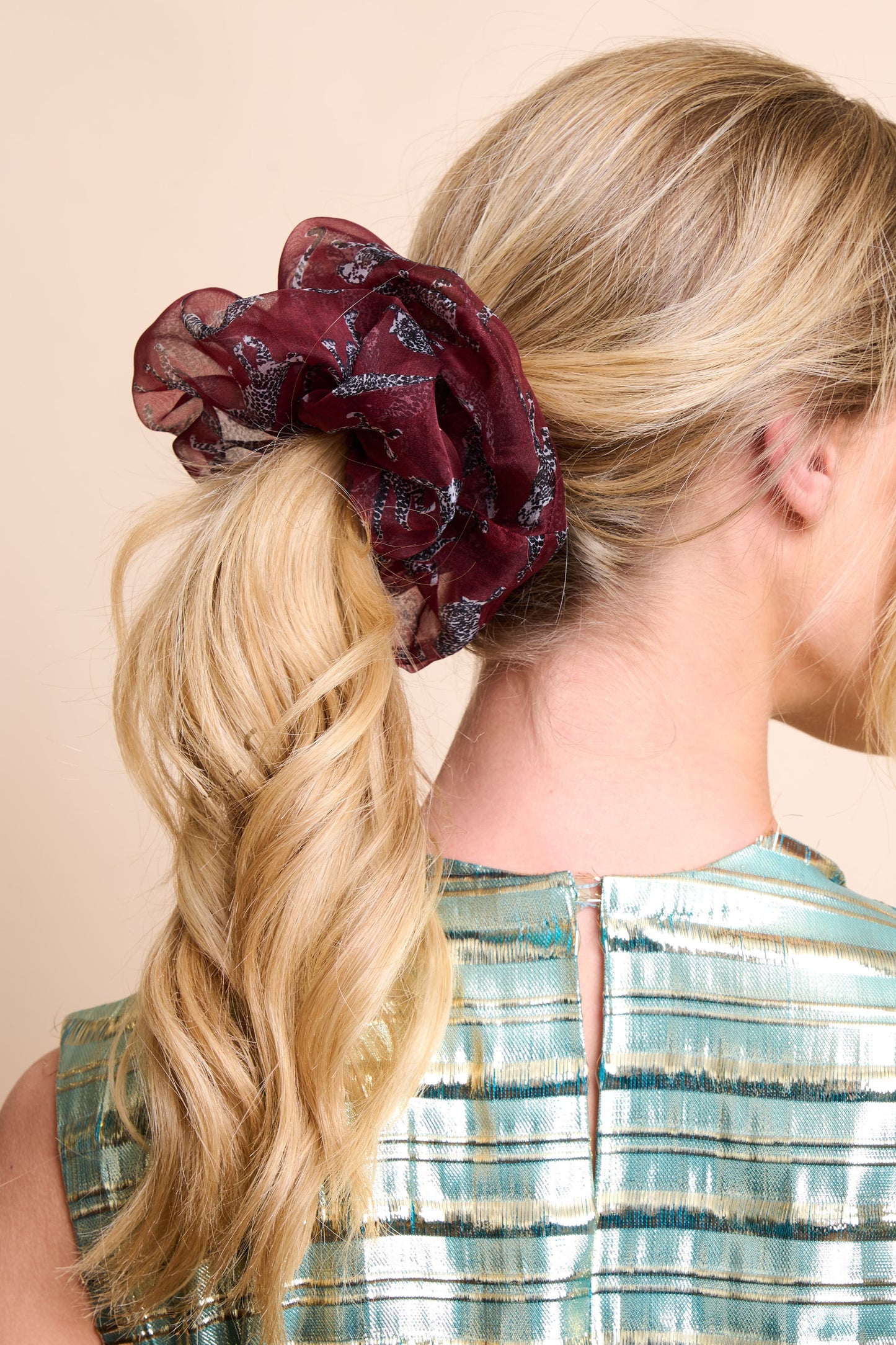 Woman with blonde hair tied in a ponytail with a burgundy silk organza scrunchie against a beige background