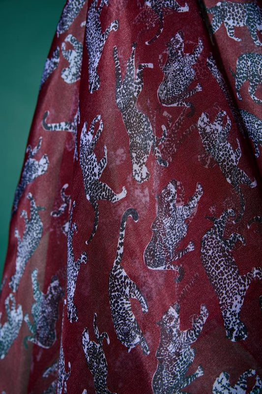 A close-up view of a burgundy silk fabric with a stylish leopard pattern. The photo shows the subtle sheerness of the material, a soft sheen, and detailed grey-toned animal motifs. This texture highlights the high quality and luxurious design of the accessory.