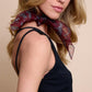 A side profile portrait of a model showcasing a narrow burgundy silk scarf with a leopard pattern. The scarf is stylishly tied around the neck, and its light, sheer fabric adds an elegant touch to the look. A black sleeveless top and a minimalist background highlight this luxurious accessory