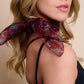 A woman wearing a bordeaux silk scarf with small cheetah patterns tied around her neck. The photo highlights the light, sheer drape of the fabric and subtle animal motifs. A minimalist look with a black sleeveless top emphasizes the elegant aesthetic of the accessory.
